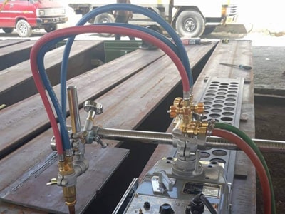 Manifold gas dengan selang merah dan biru di meja kerja, dengan truk di latar belakang.
