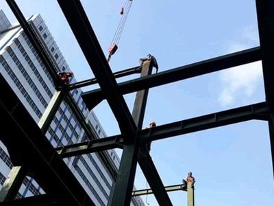 Pekerja konstruksi pada balok baja rangka bangunan dengan latar langit biru.