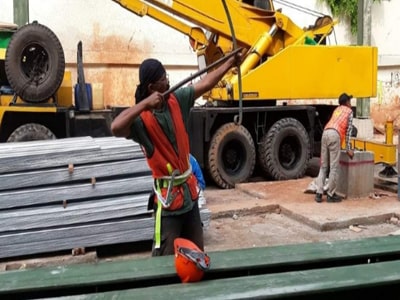 Pekerja konstruksi pada balok baja rangka bangunan dengan latar langit biru.