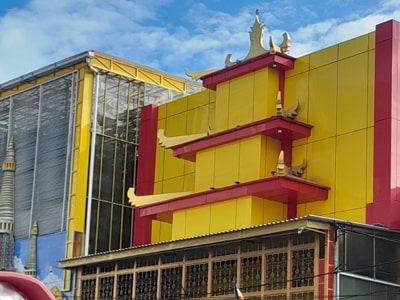 Bangunan modern dengan fasad merah dan kuning serta detail arsitektur Asia dengan latar langit biru.
