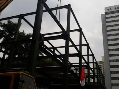 Lokasi konstruksi dengan rangka baja dan bendera di depan gedung tinggi.